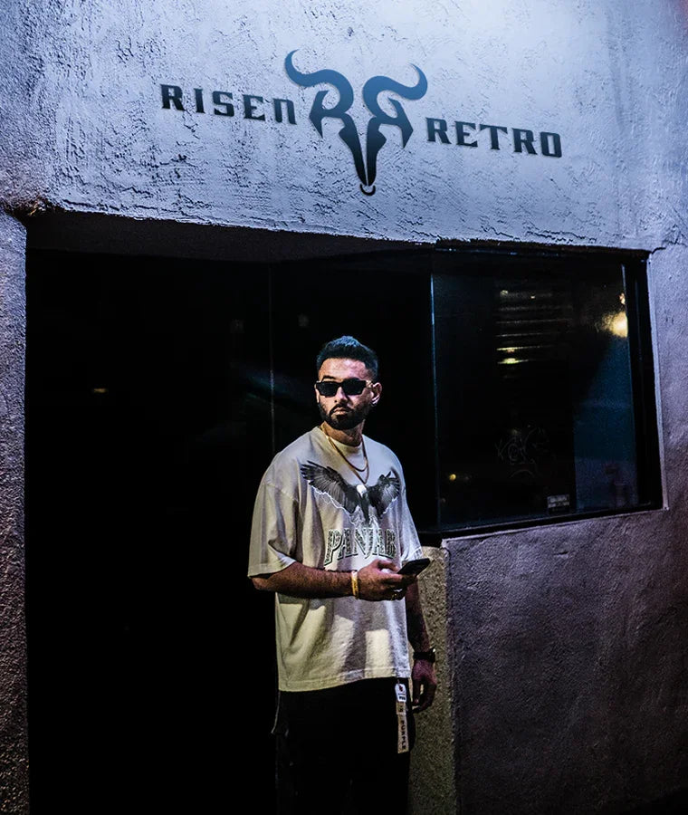 Man in oversized Punjabi streetwear t-shirt with bold graphic, standing under urban signage at night